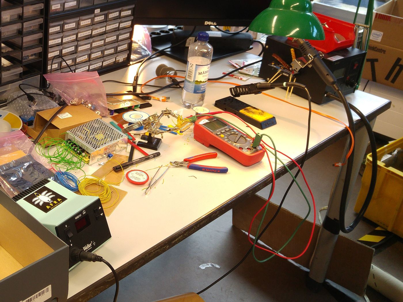 An electronics bench with a multimeter, soldering station, and hand tools